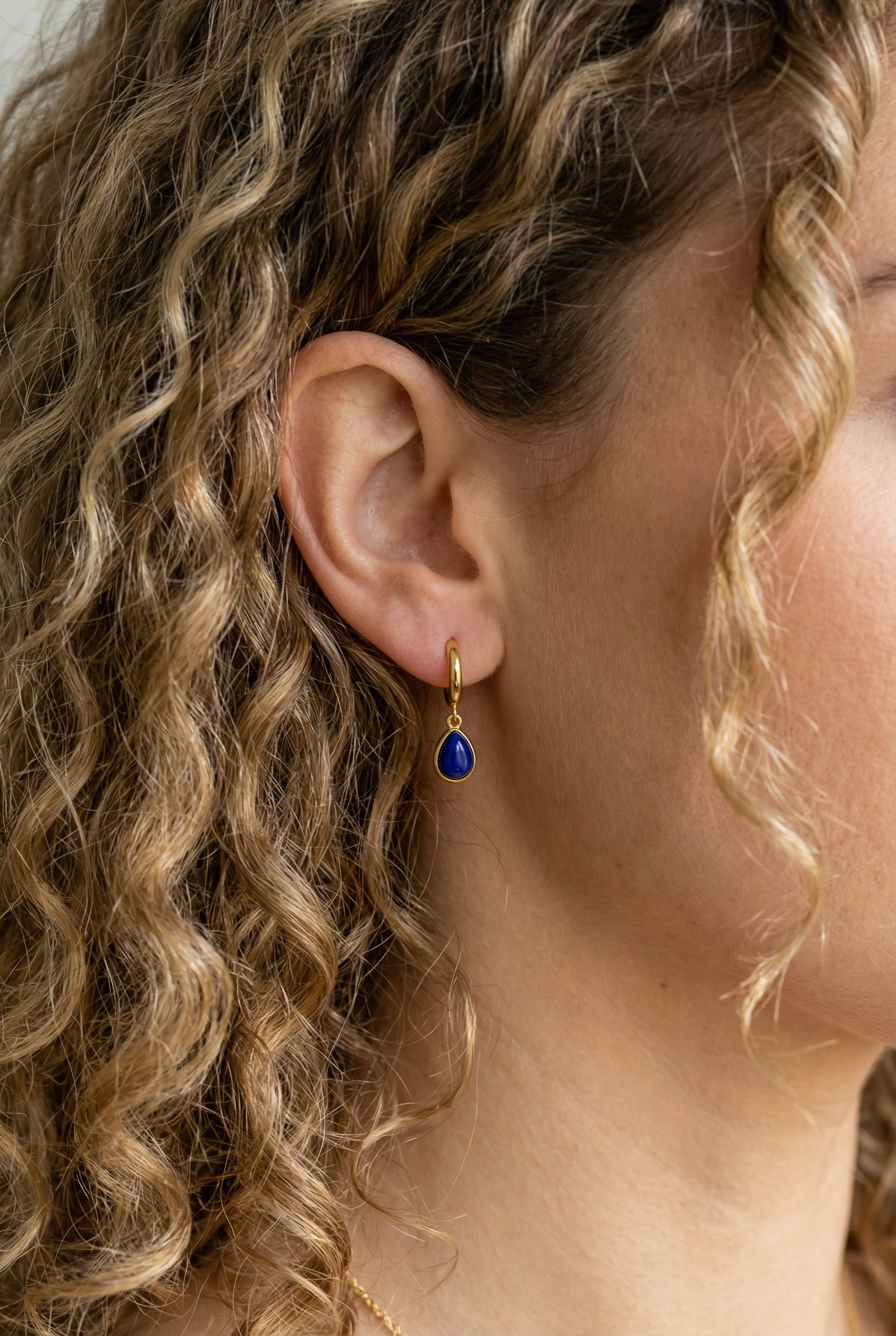 Ohrringe Sarah – Model mit lockigem Haar trägt vergoldete Creole mit blauem Lapislazuli